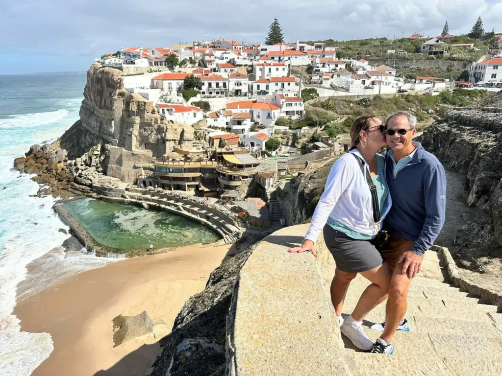 Couple enjoying the view at Azenhas do Mar, a stunning cliffside village near Sintra, Portugal, during a tour with the company Yes, You Deserve. The ocean, natural pool, and traditional white houses with red roofs create a picturesque backdrop.