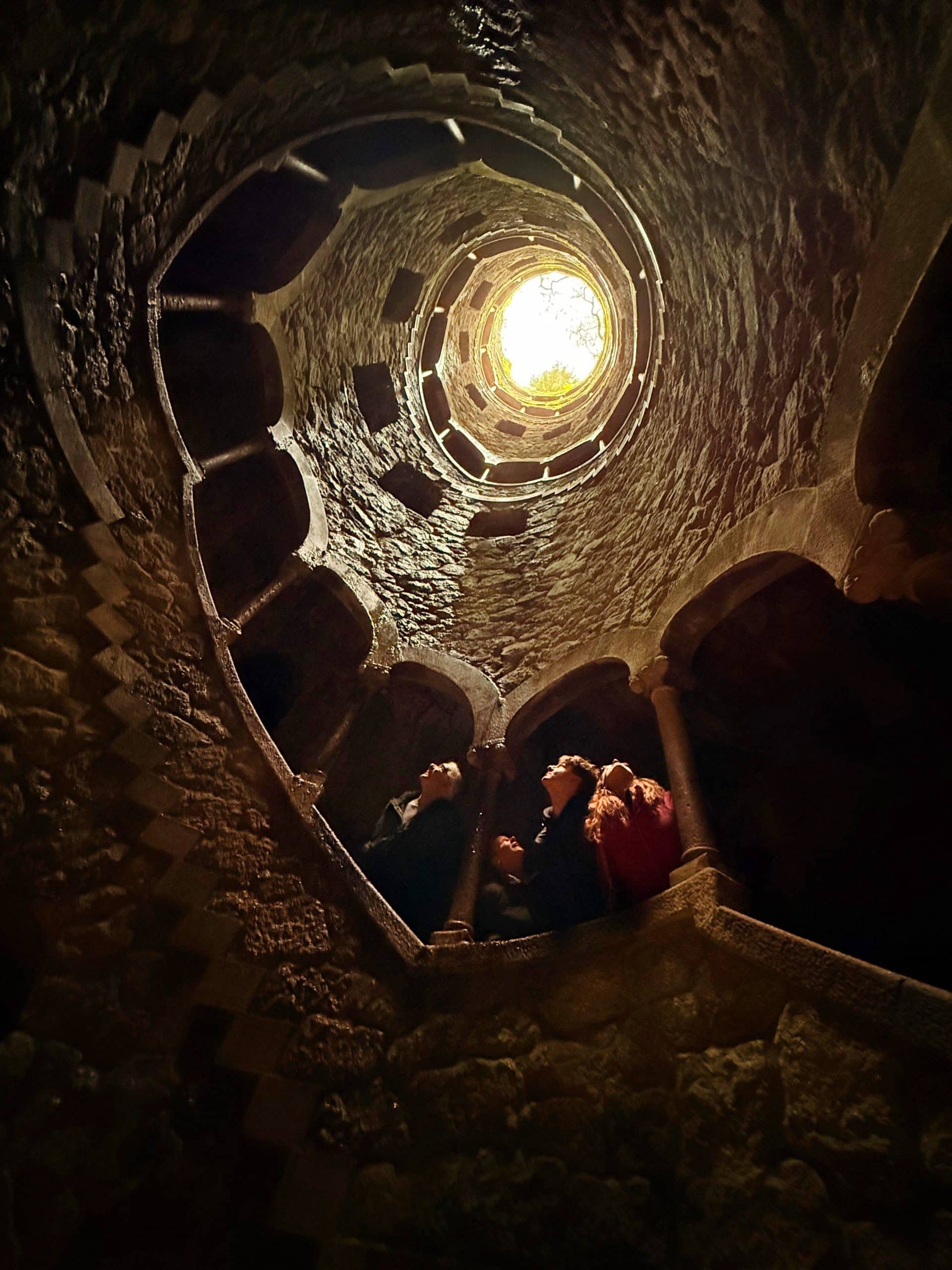 Stone stairs and arched galleries spiralling around Regaleira’s Initiation Well, viewed from below