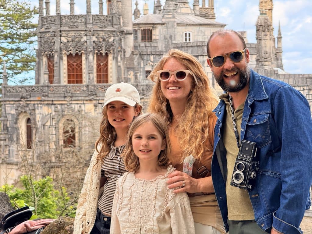 Family posing together outdoors in front of a historic stone castle, smiling at the camera.