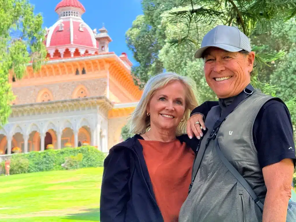 Smiling couple posing outdoors with an ornate orange-domed building and trees in the background.