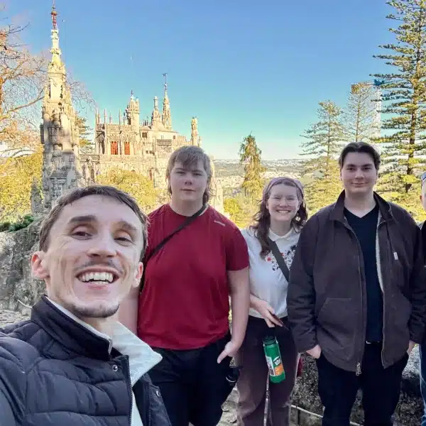 Tour guide with smiling visitors at Quinta da Regaleira in Sintra, Portugal, with the gothic-style palace in the background on a clear day.