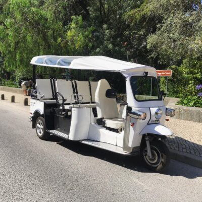 A white electric tuk-tuk parked on a quiet road in Sintra, Portugal, ready to take guests on a scenic and eco-friendly adventure with Yes, You Deserve. Surrounded by lush greenery and cobblestone paths, it offers a charming and sustainable way to explore the town.