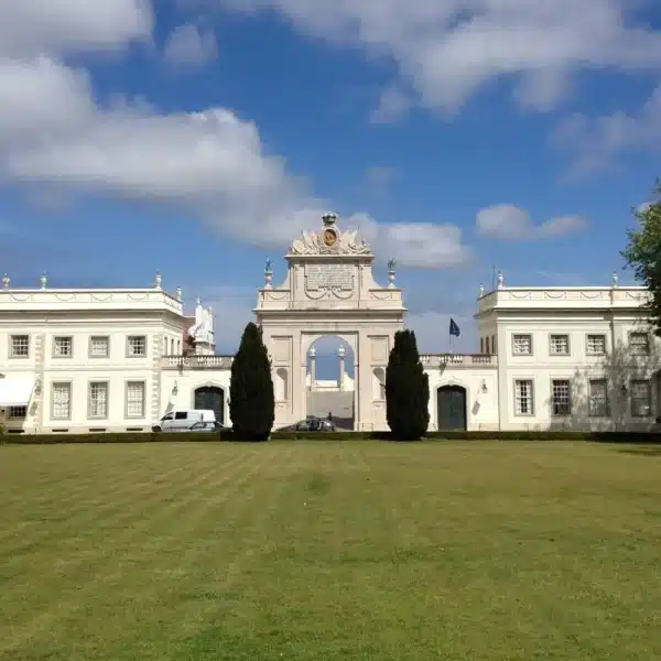 Front view of Palรกcio de Seteais in Sintra, Portugal, with neoclassical architecture, central archway, manicured lawn, and blue sky โ luxury hotel Tivoli Palรกcio de Seteais.