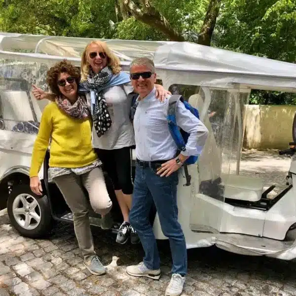 Happy tourists posing next to an electric tuk tuk in Sintra, Portugal during a private guided tour with Yes, You Deserve โ a fun and comfortable way to explore the regionโs top landmarks with a local expert.