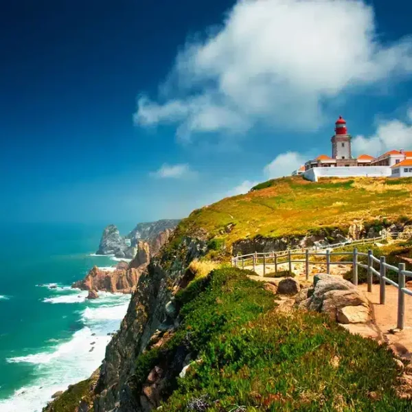 Scenic view of Cabo da Roca, the westernmost point of continental Europe, featuring dramatic cliffs, the Atlantic Ocean, and a historic lighthouse under a vibrant blue sky. A popular stop on the Yes, You Deserve Sintra and coastal tour.